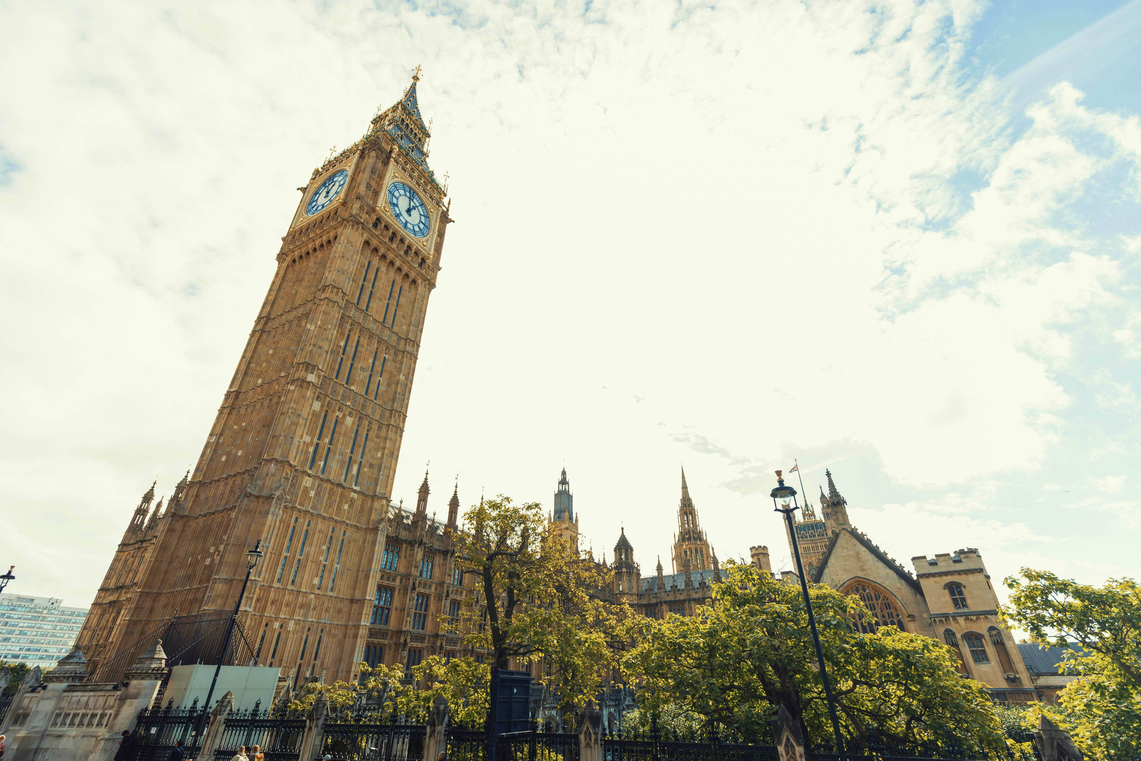 Big Ben clock tower and Houses of Parliament with green trees in London under cloudy sky